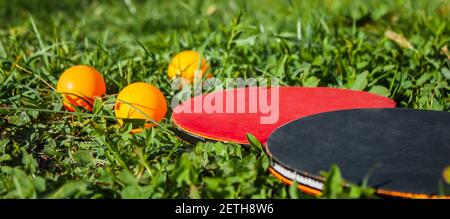 Deux raquettes de tennis de table et trois balles d'orange se trouvent dans l'herbe. Le concept des jeux de sports de plein air Banque D'Images