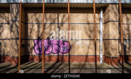 Graffitis sur un bâtiment abandonné pris par une clôture rouillée. Banque D'Images