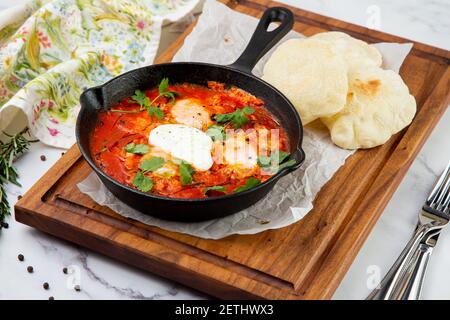 shakshuka - oeufs brouillés aux herbes, haricots et tomates dans une poêle à pain croustillant Banque D'Images