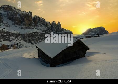 Cabane en bois recouverte de neige avec Sassolungo en arrière-plan au coucher du soleil, Passo Gardena, Dolomites, Tyrol du Sud, Italie Banque D'Images