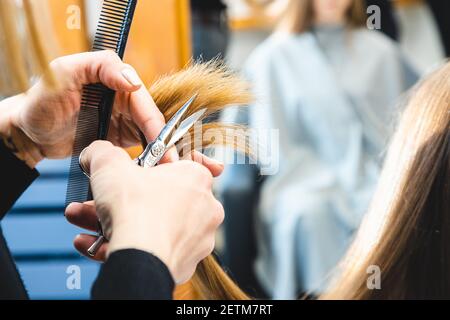 Le coiffeur principal coupe les extrémités des cheveux de la fille après avoir lavé le salon de beauté en gros plan Banque D'Images