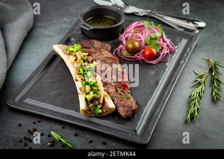 steak de bœuf avec sucre d'os, servi avec de la sauce et une salade d'oignons, de pomileurs et de poivrons. fond sombre Banque D'Images