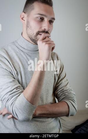 Portrait d'un jeune homme avec une barbe courte piquant ses ongles pensant sérieusement Banque D'Images