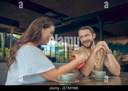 Femme ouvrant cadeau et homme joyeux dans le café Banque D'Images