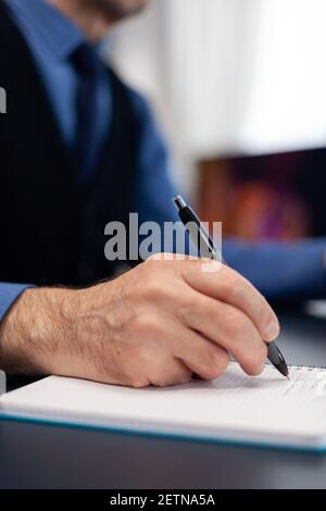 Gros plan sur un homme qui prend des notes sur un ordinateur portable tout en travaillant à la maison. Homme âgé entrepreneur dans le lieu de travail à la maison utilisant un ordinateur portable assis au bureau tandis que la femme lit un livre assis sur le canapé. Banque D'Images