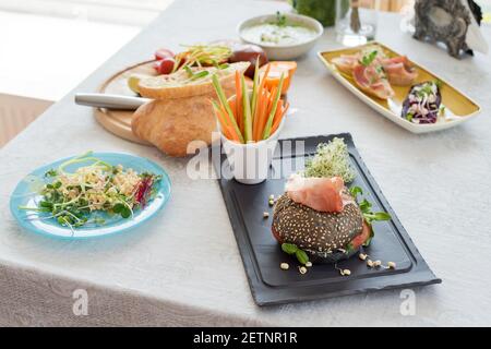 Hamburger sain avec du hamon, des tomates, des micro-légumes verts et des petits pains de wholegrain noirs, des bâtonnets de légumes sur la table. Cuisson avec des micro-verts. Manger propre Banque D'Images