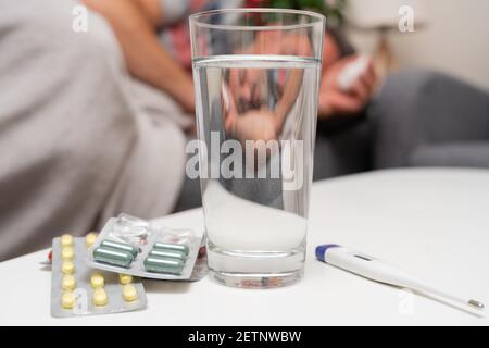 Gros plan de la médecine de traitement du froid verre d'eau et numérique thermomètre sur la table comme grippe influneza concept d'infection avec malade homme adulte dormant Banque D'Images