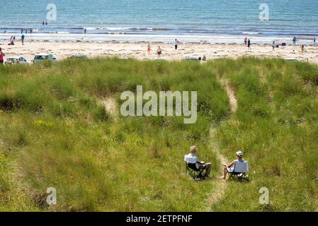 Un couple de personnes âgées assis sur des chaises longues dans une dune de sable par un chemin menant à la plage. Retraités sur la plage. Inch Beach, comté de Kerry, Irlande Banque D'Images