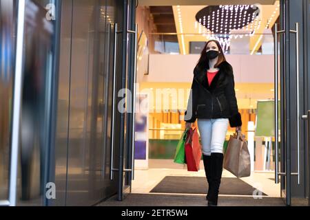 Belle femme dans un masque de protection avec des sacs de shopping sort du centre commercial. Cabas élégant fille Banque D'Images