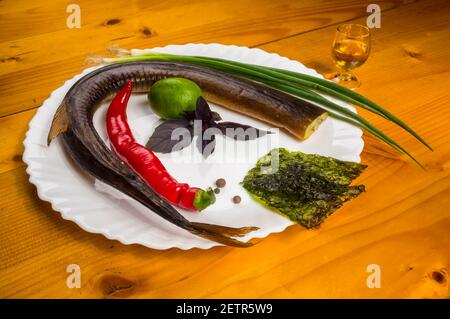 Still Life - orphie fumé avec de la chaux, le basilic, l'oignon vert, chili, nori chips, épices, huile d'olive dans un plat de céramique blanc, sur une table en bois Banque D'Images