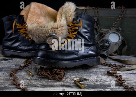 Bottes en cuir avec chaînes rouillées et coques ogive avec militaire masque à gaz et manteau de fourrure en arrière-plan reposant sur du bois tableau Banque D'Images