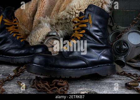 Bottes en cuir avec chaînes rouillées et coques ogive avec militaire masque à gaz et manteau de fourrure en arrière-plan reposant sur du bois tableau Banque D'Images