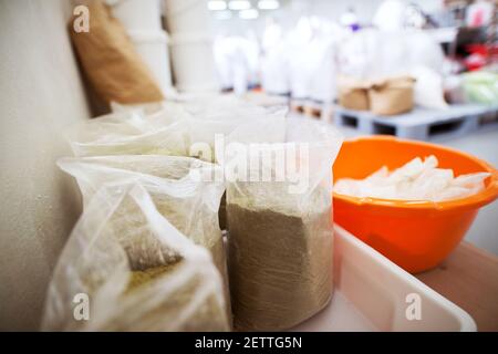 Gros plan sur les sacs transparents en plastique remplis d'épices vertes près du bassin en plastique orange de l'usine de production alimentaire. Banque D'Images