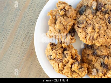 Vue panoramique sur une assiette blanche avec biscuits aux raisins secs faits maison à l'avoine et dont un cassé éclairé par la lumière naturelle. Banque D'Images