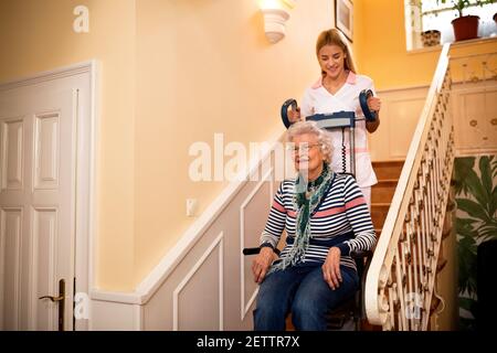 Vieille dame souriante, heureuse pendant que l'infirmière l'aide à monter dans les escaliers à la maison de soins infirmiers Banque D'Images