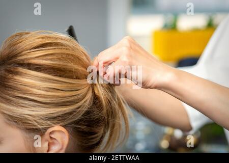 Gros plan de coiffeur femme coiffant les cheveux blonds d'un jeune femme dans un salon de beauté Banque D'Images