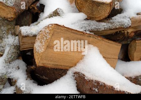 Bois de chauffage fendu de feuillus et de résineux recouvert de neige en hiver pendant le séchage. Banque D'Images