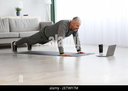 Sportif homme mature faisant des exercices à la maison, à l'aide d'un ordinateur portable Banque D'Images