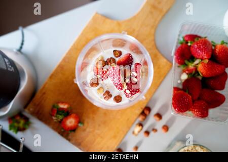 Au-dessus de la vue du bol mélangeur rempli de fraises au lait frais et de noisettes prêtes à être préparées en smoothie. Banque D'Images