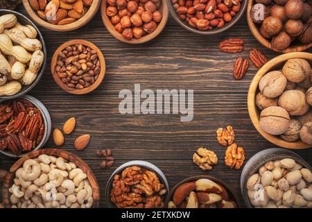 Assortiment de noix dans des bols. Noix de cajou, noisettes, noix, pistaches, pacanes, pignons de pin, arachides, macadamia, amandes, noix du brésil. Mélange alimentaire sur bois Banque D'Images