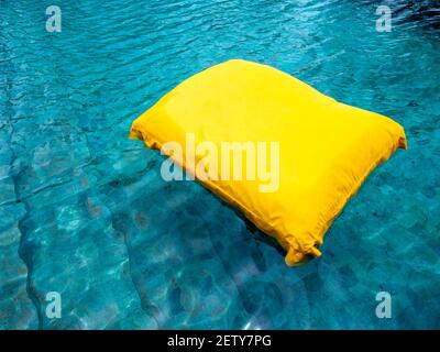 Un grand oreiller jaune flottant dans la piscine. Lit flottant sur l'eau. Banque D'Images