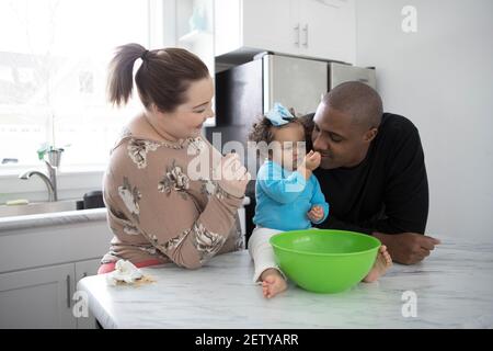 Un heureux couple interracial dans une cuisine moderne avec leur petite fille. Banque D'Images