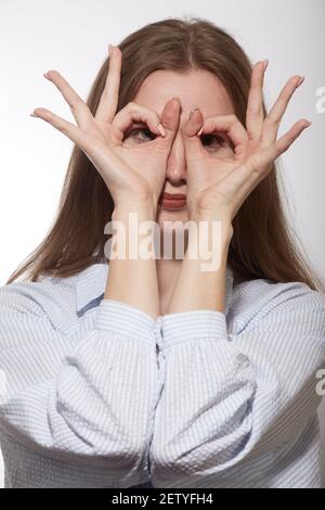 Young woman looking at camera entre ses doigts avec lunettes geste sur fond blanc Banque D'Images