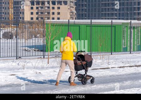 Femme marchant et poussant un landau ou une poussette sur une route enneigée et glacée dans la ville d'hiver. Banque D'Images