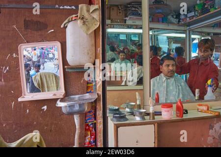 Les miroirs d'un salon de coiffure à Mumbai, en Inde, reflètent le coiffeur et le client plusieurs fois, tandis qu'un autre miroir reflète la vie de la rue à l'extérieur Banque D'Images