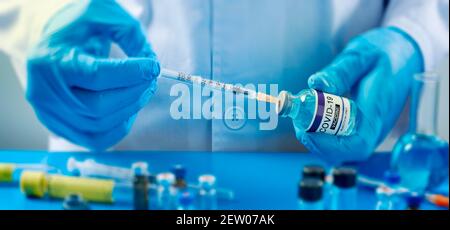 gros plan d'un travailleur de la santé ou d'un laboratoire, portant des gants bleus, remplissant une seringue d'un flacon simulé de vaccin covid-19, sur une table Banque D'Images