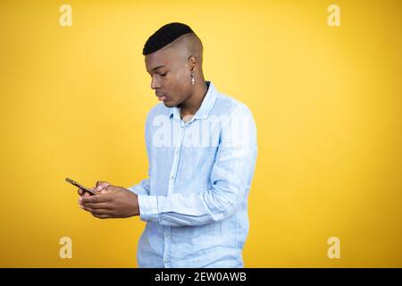 Jeune homme afro-américain portant une chemise décontractée conversation sur fond jaune sur le téléphone Banque D'Images