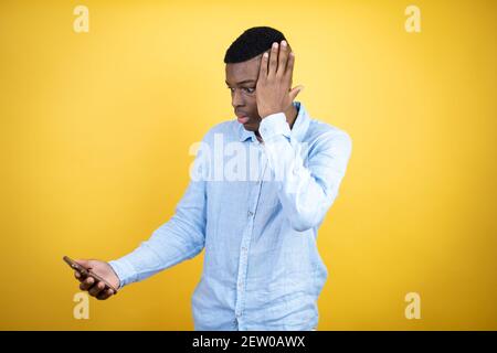 Jeune homme afro-américain portant une chemise décontractée arrière-plan jaune discutant sur le téléphone avec une expression inquiète Banque D'Images