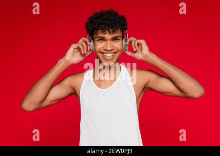 joyeux afro-américain qui règle les écouteurs sans fil isolés sur le rouge Banque D'Images