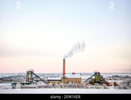 Ancienne mine de charbon en fonctionnement dans le paysage rural avec la fumée de la cheminée de la roue de bobinage de la maison de moteur de colliery. Sous la neige de Noël hiver Banque D'Images