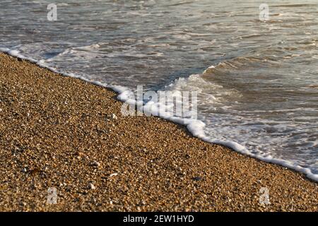 Gros plan sur une plage de galets éclairée par un doré brillez avec de légères vagues au bord de l'eau un arrière-plan paisible en bord de mer Banque D'Images