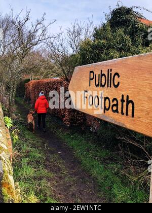 Un marcheur de chien marchant son chien le long d'un sentier public Avec un panneau indiquant le chemin à travers la campagne anglaise Banque D'Images