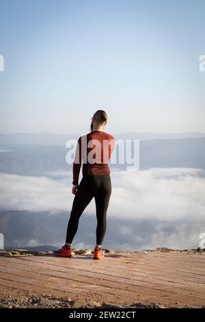 Athlète masculin debout sur un sommet de montagne regardant au-dessus de la nuages épais Banque D'Images