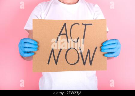 Message carton avec ACT NOW. Les mains anonymes protégées avec des gants tiennent l'affiche de protestation Banque D'Images