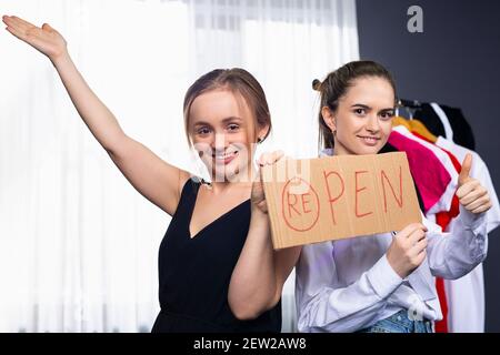 Deux femmes heureuses assises dans leur boutique et accrochant une AFFICHE OUVERTE sur la porte. Le propriétaire d'une petite entreprise qui met un panneau ouvert sur la porte en face de Banque D'Images