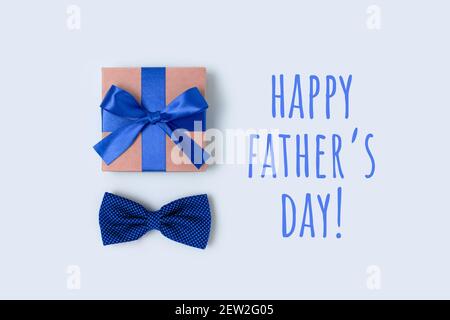 Bonne journée des Pères. Placette festive avec boîte cadeau et noeud papillon. Cadeau attaché avec un ruban sur fond bleu pastel. Banque D'Images
