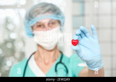Cardiologue tenant le cœur rouge dans un gant de protection Banque D'Images