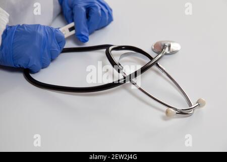 Les mains avec des gants bleus du médecin tiennent un thermomètre électronique. Banque D'Images