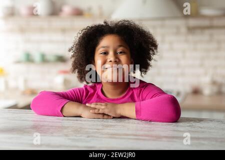 Gros plan Portrait d'une petite fille noire en forme de curly, assise à une table Dans la cuisine Banque D'Images