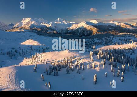 Vue aérienne du paysage d'hiver avec forêt enneigée dans les montagnes avec belle lumière de coucher de soleil. Banque D'Images