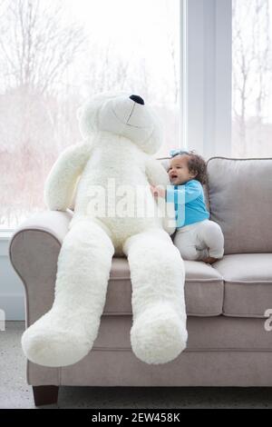 Une petite fille est assise sur un canapé avec un ours en peluche blanc géant. Banque D'Images