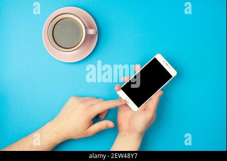 Mockup - la main de l'homme tient un smartphone sur fond bleu et une tasse de café. Placer pour le texte Banque D'Images