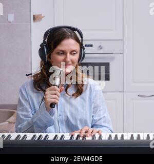 Bonne femme musicienne dans un casque avec microphone jouant électrique à la maison piano Banque D'Images