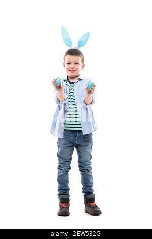 Enfant frais avec des oreilles de lapin qui rigolent et sourient avec des œufs peints de Pâques. Corps entier isolé sur fond blanc. Banque D'Images