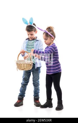 Jeux de Pâques d'enfance. Deux petits enfants garçon et fille tenant le panier à la recherche d'oeufs peints. Corps entier isolé sur fond blanc. Banque D'Images