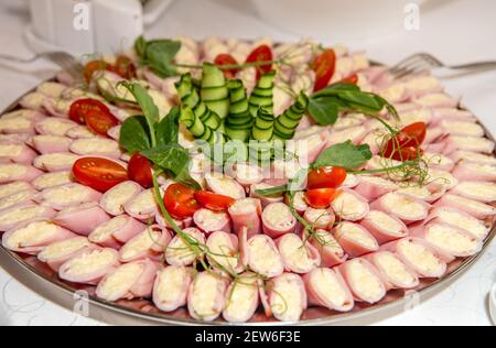 Encas roulés au jambon et au fromage râpé servis sur un grand plateau à l'intérieur. Concept d'en-cas de fête sans gluten. Banque D'Images